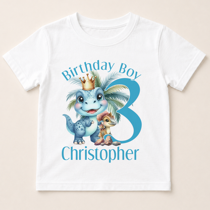 A white t-shirt with a graphic design featuring a dinosaur wearing a crown and the text "Birthday Boy Christopher" along with a number 3.