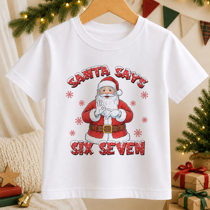 A white t-shirt with a graphic design featuring a cartoon Santa Claus holding a sign that says "Santa Says Six Seven".