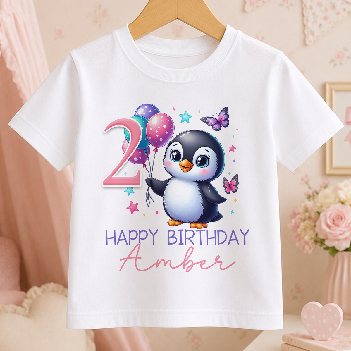 A white t-shirt with a cartoon penguin and balloons, along with the text "Happy Birthday Amber" printed on it.