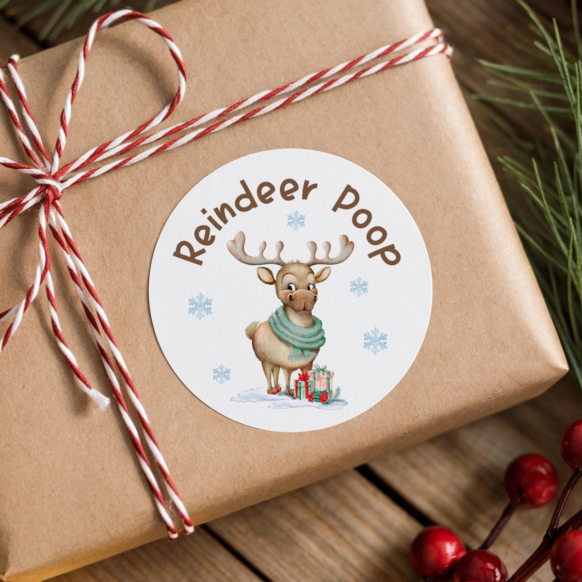 Personalised Reindeer Poop Christmas sticker with custom name on a wrapped gift box with pine branches and berries