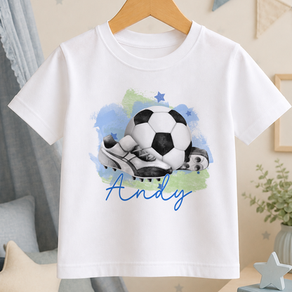 A white t-shirt with a printed design of a soccer ball and cleats, along with the name "Andy" written below the image.