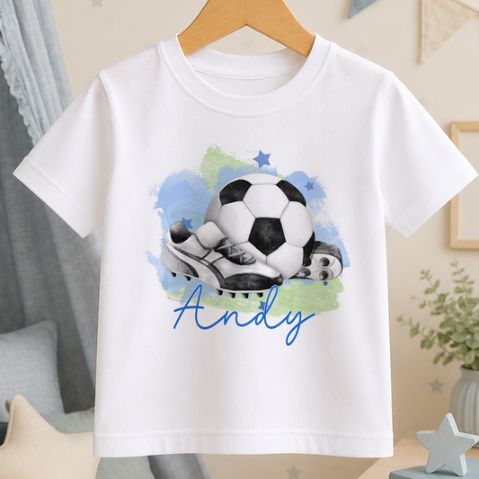 A white t-shirt with a printed design of a soccer ball and cleats, along with the name "Andy" written below the image.