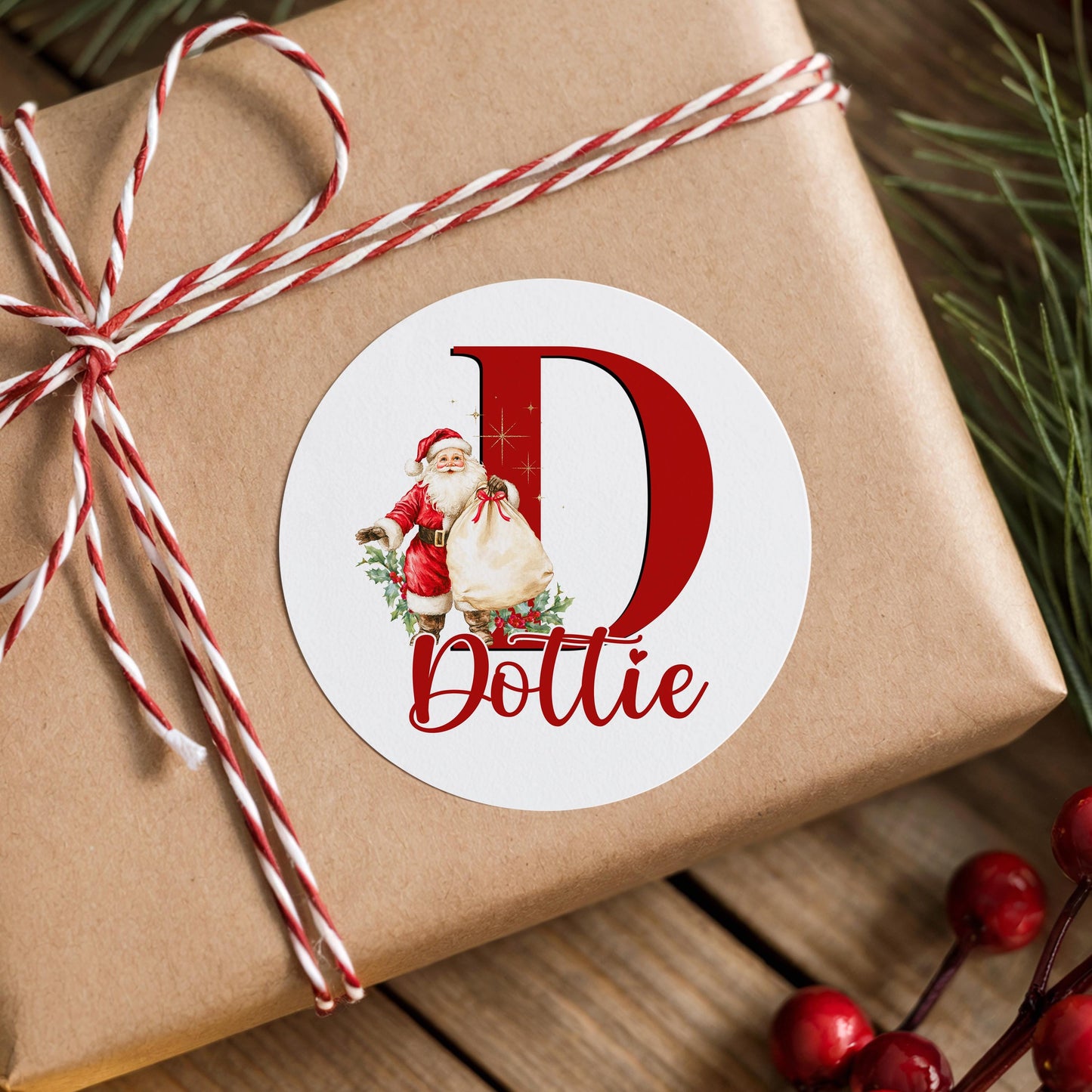 Personalised vintage Santa initial sticker with a large red letter and custom name in script, shown on a wrapped Christmas gift