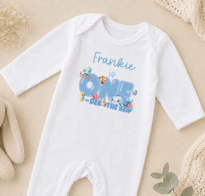 A white onesie with a personalized text and illustrations related to the ocean theme, specifically "Frankie is ONE DER THE SEA".