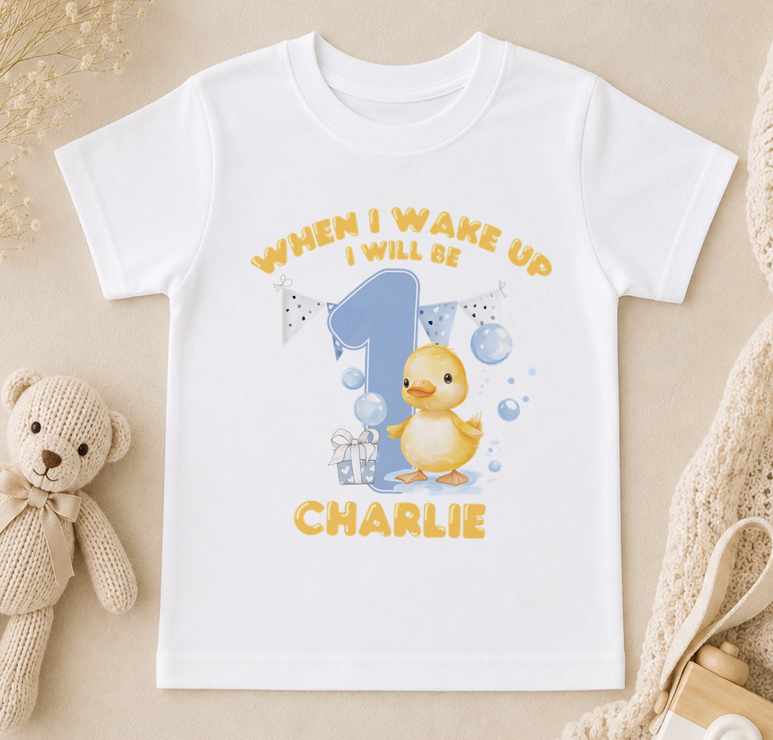 A white t-shirt with a cartoon image of a yellow duck and the text "When I wake up I will be Charlie" printed on it.
