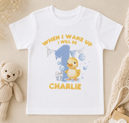 A white t-shirt with a cartoon image of a yellow duck and the text "When I wake up I will be Charlie" printed on it.