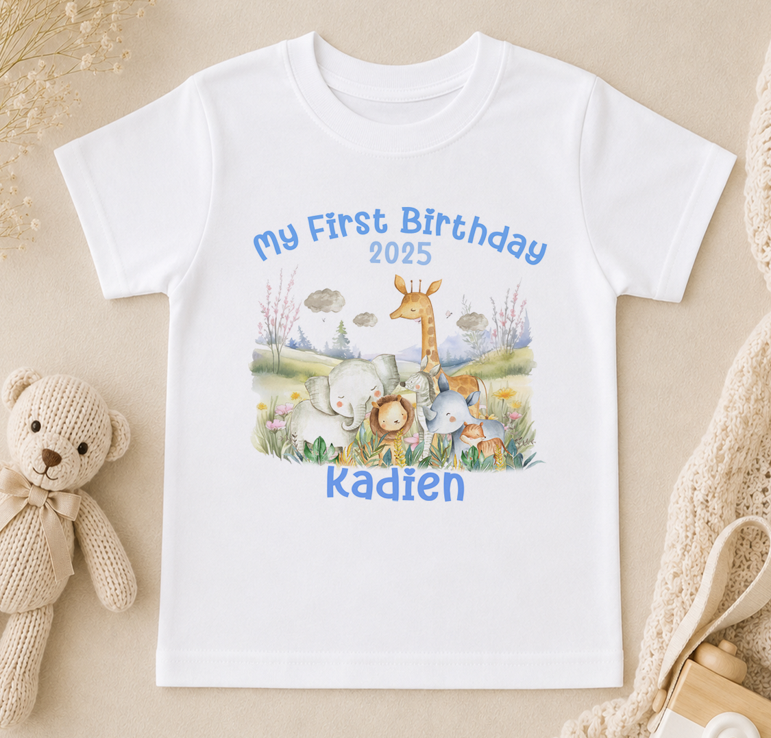 A white t-shirt with a printed design of various animals, including elephants, giraffes, and a teddy bear, along with the text "My First Birthday 2020 Kadien".