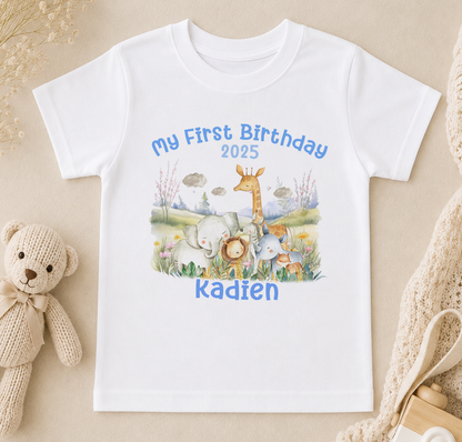 A white t-shirt with a printed design of various animals, including elephants, giraffes, and a teddy bear, along with the text "My First Birthday 2020 Kadien".