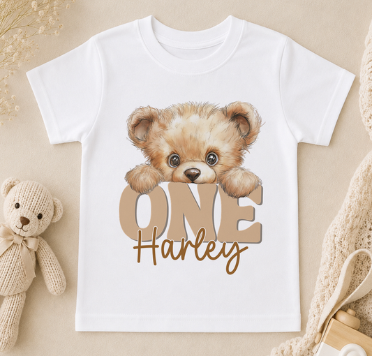 A white t-shirt with a teddy bear and the text "ONE Harley" printed on it, along with a small stuffed bear.