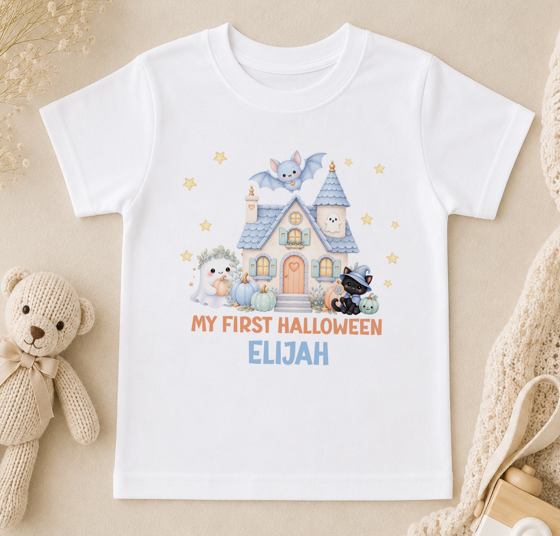 A white t-shirt with a Halloween-themed graphic design, including a house, bats, and a teddy bear, along with the text "My first Halloween Elijah".