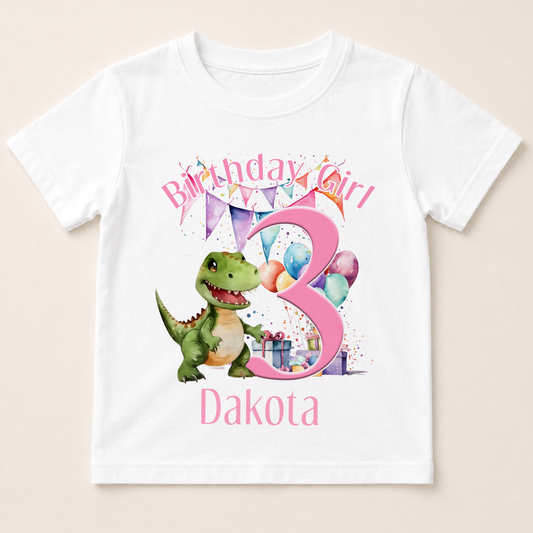 A white t-shirt with a birthday girl design, featuring a green dinosaur, balloons, and the number 3.