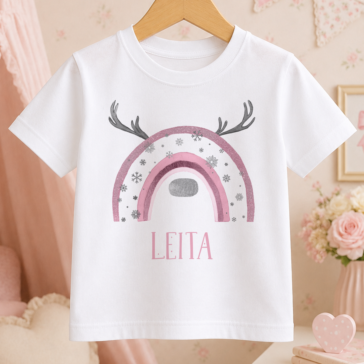 A white t-shirt with a pink and silver design featuring a rainbow and antlers, along with the name "LEITA" printed on it.