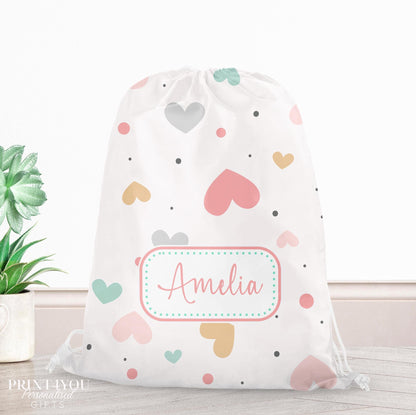 Personalised pastel heart print drawstring PE bag in pink, mint, mustard and grey, printed with a custom name on the front