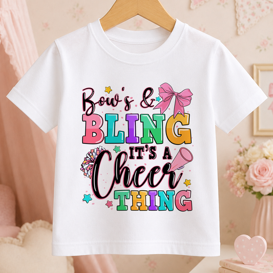 A white t-shirt with a colorful graphic design that says " Bow's & Bling It's a Cheer Thing" printed on it.