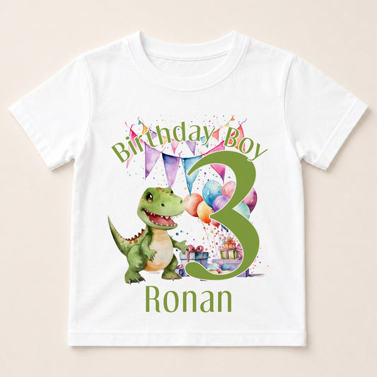 A white t-shirt with a graphic design featuring a green dinosaur and colorful balloons, along with the text "Birthday Boy Ronan" and the number "3".