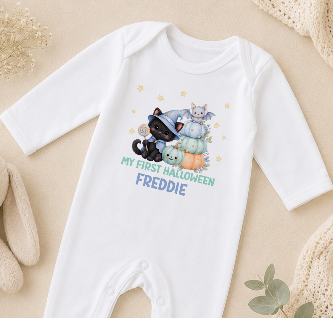 A white onesie with a Halloween-themed design, featuring a witch, a cat, and pumpkins, along with the text "My first Halloween Freddie".