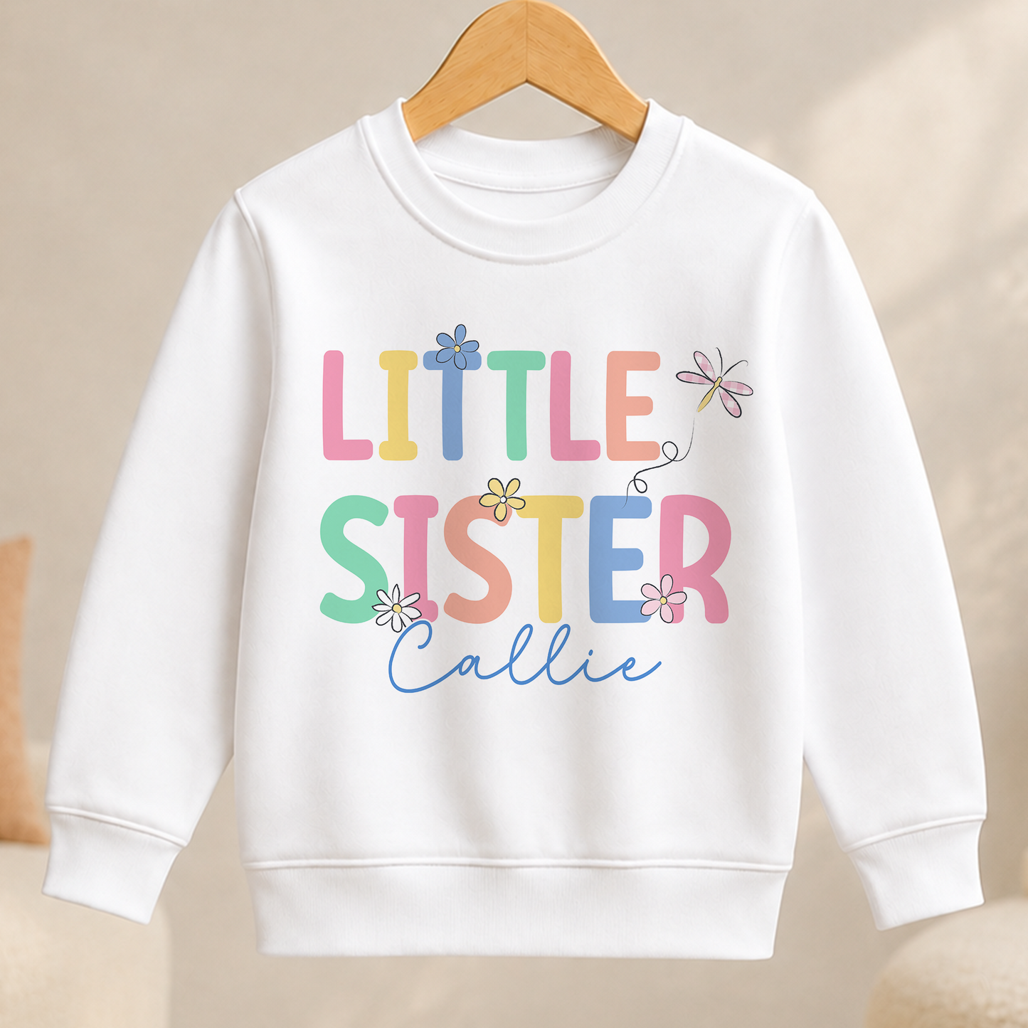 A white children's sweatshirt with the text "Little Sister" and a flower design printed on it.