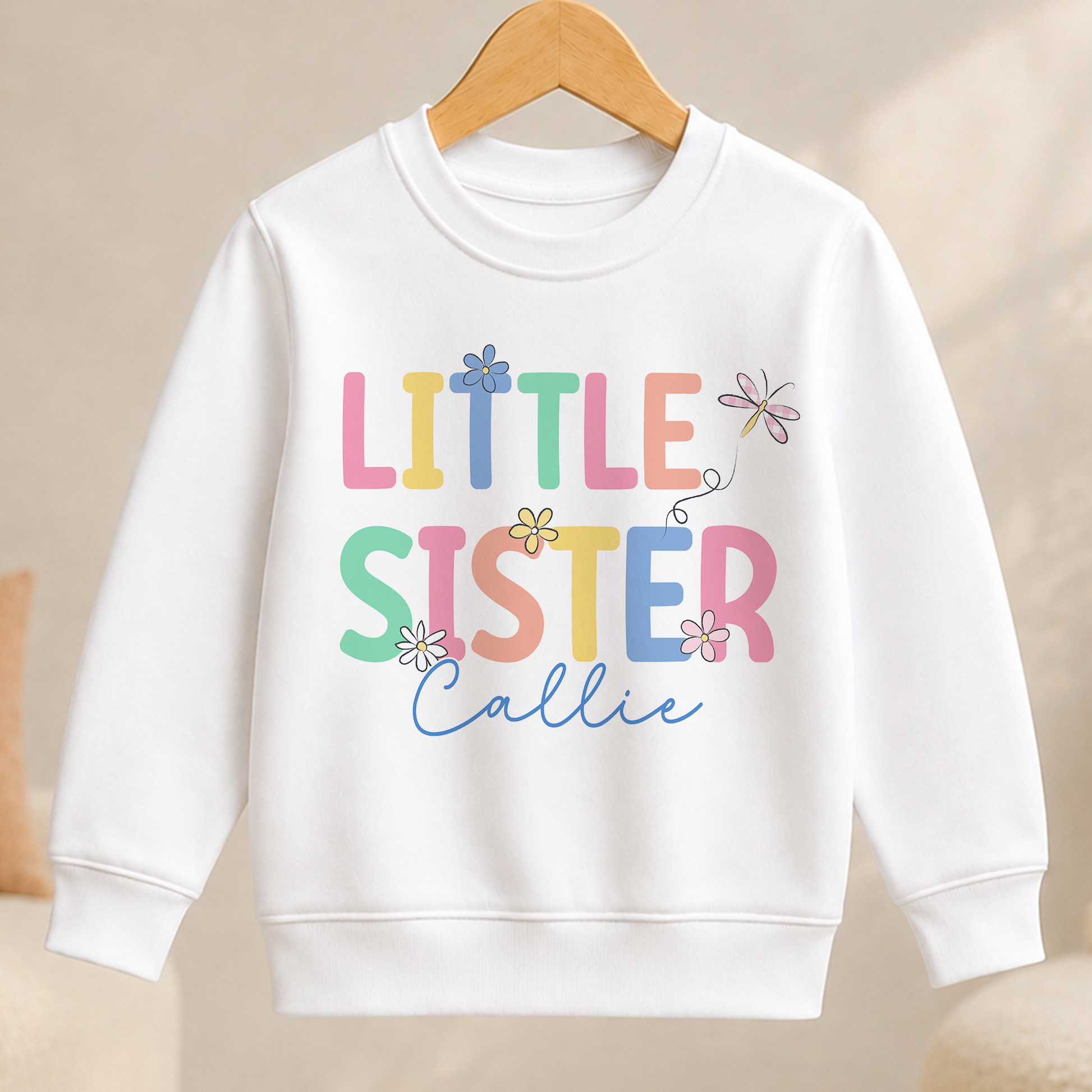 A white children's sweatshirt with the text "Little Sister" and a flower design printed on it.