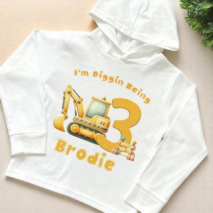 Birthday Digger personalised long-sleeved hooded t-shirt in white jersey cotton, 6-12 months size, front view showing digger birthday number design
