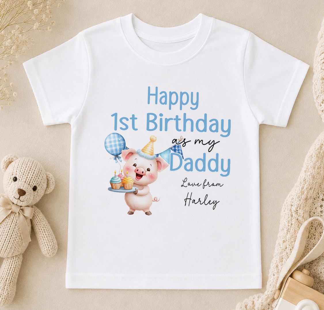 A white t-shirt with a cartoon image of a pig holding a birthday cake and balloons, along with text that reads "Happy 1st Birthday as my Daddy Love from Harley".