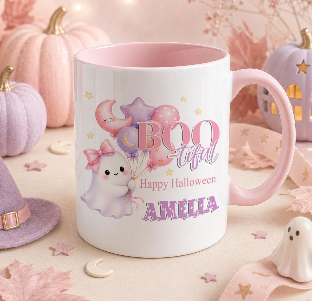 White ceramic mug with pink handle and pink inner, printed with a pastel pink ghost holding balloons, Boo-tiful text and the personalised name Amelia, styled with mini pumpkins for Halloween.