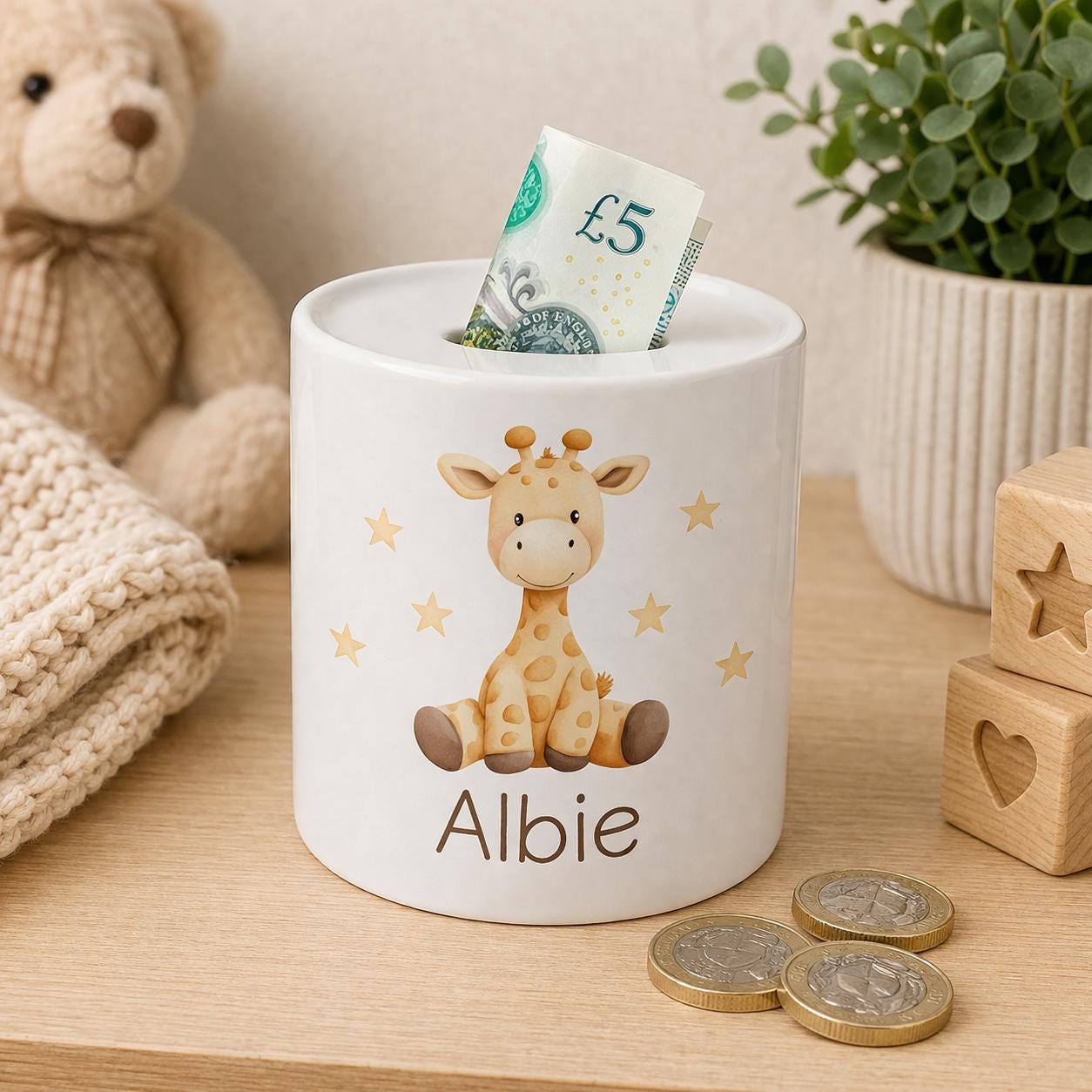 Ceramic giraffe money box with a baby giraffe and gold star illustration, personalised name in brown script, styled with a plush giraffe toy and coins