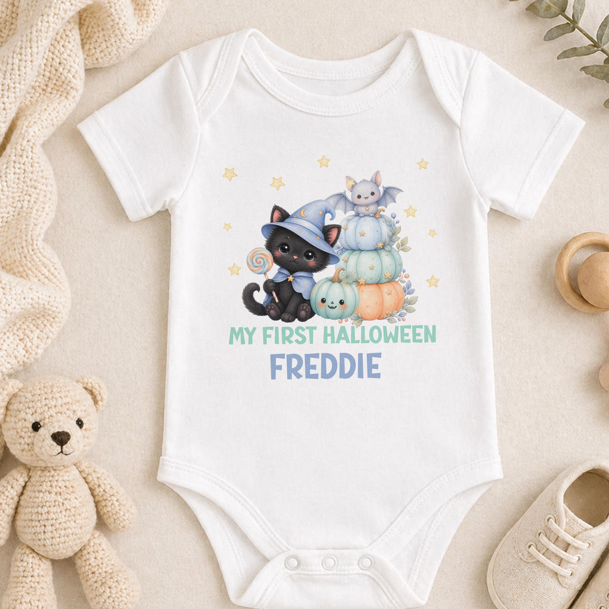 Personalised baby's first Halloween outfit with a black kitten in a wizard hat, pastel pumpkins, a bat and the baby's name in blue and teal.