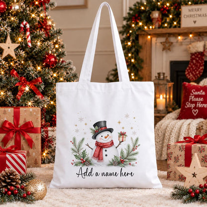 Personalised white cotton tote bag with a watercolour snowman in a top hat and red scarf, holly, berries and a name below