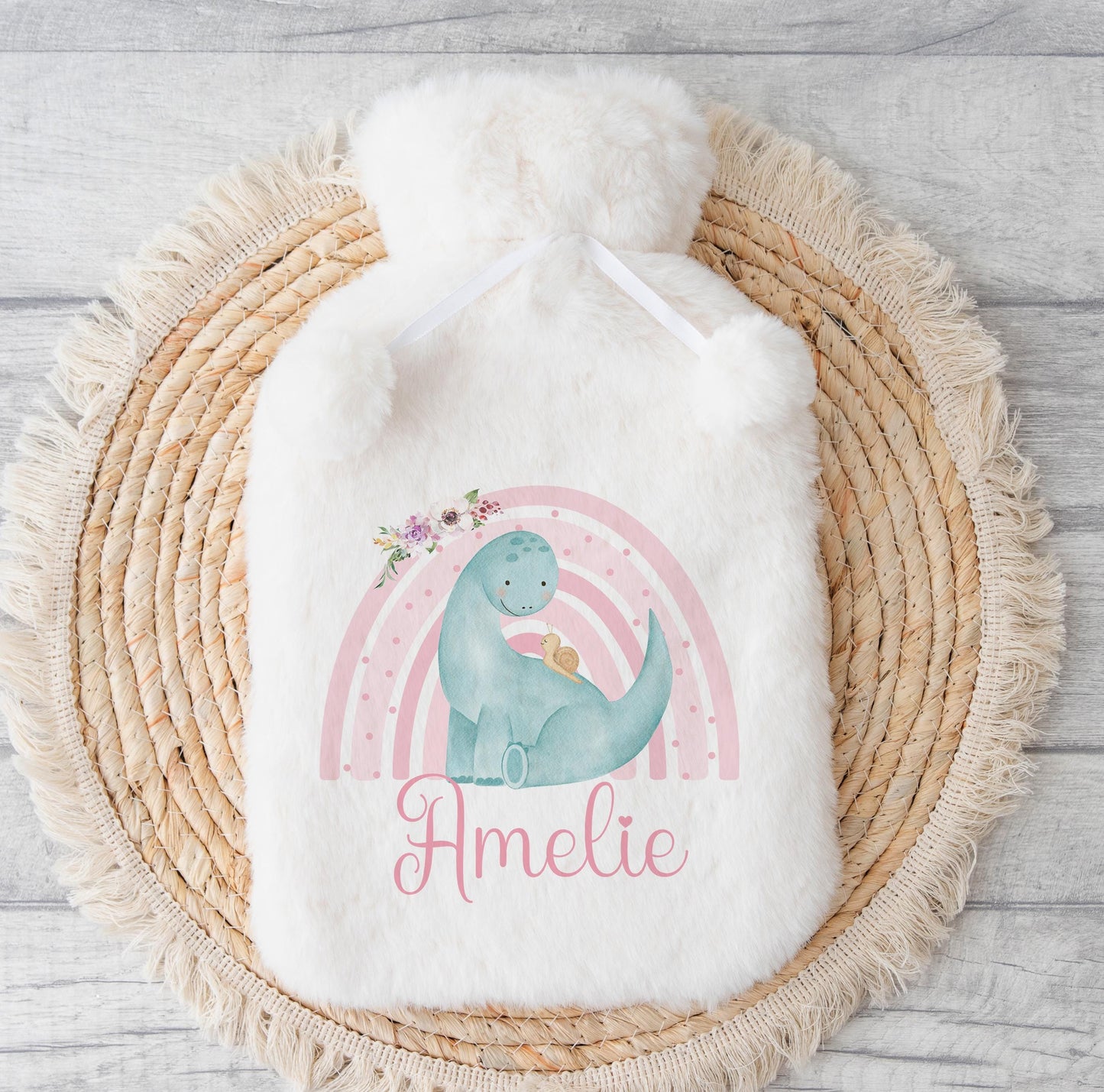 Fluffy white hot water bottle cover with a pastel rainbow dinosaur design, printed with the personalised name Amelie