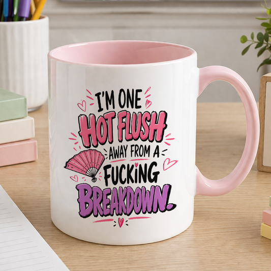White ceramic mug with a pink handle and pink interior, printed with the slogan 'I'm one hot flush away from a fucking breakdown'.