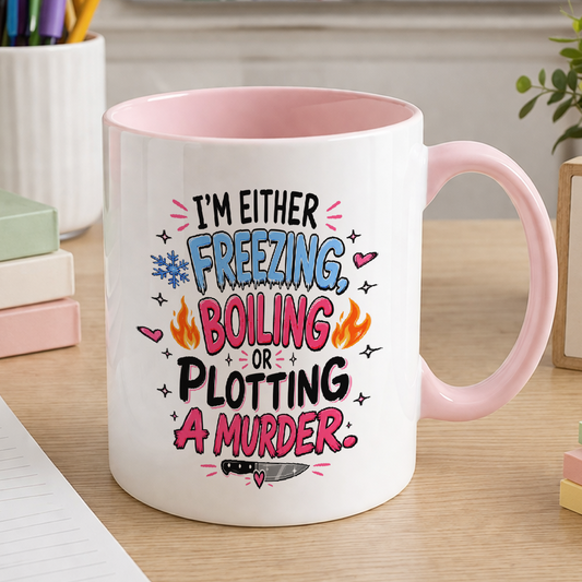 White ceramic mug with pink handle and pink inner, printed with the text I'm either freezing, boiling or plotting a murder