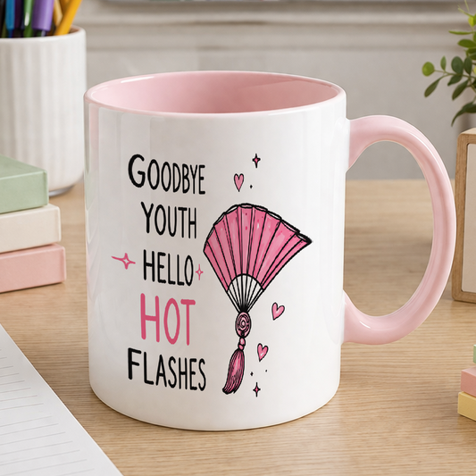 White ceramic mug with a pink handle and pink interior, printed with the slogan 'Goodbye youth, hello hot flashes'.