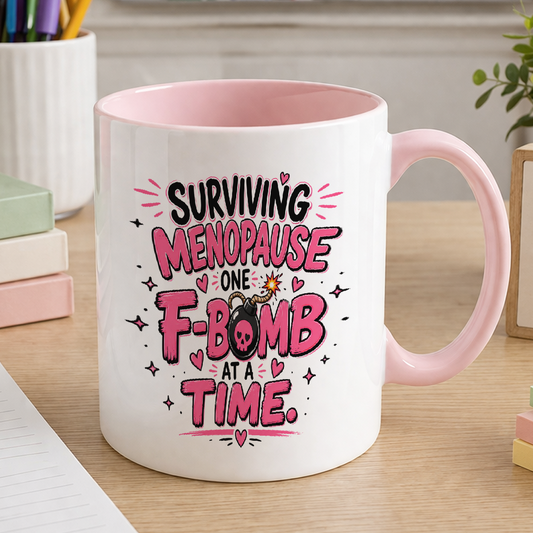 White ceramic mug with pink handle printed with the slogan Surviving menopause one F-bomb at a time