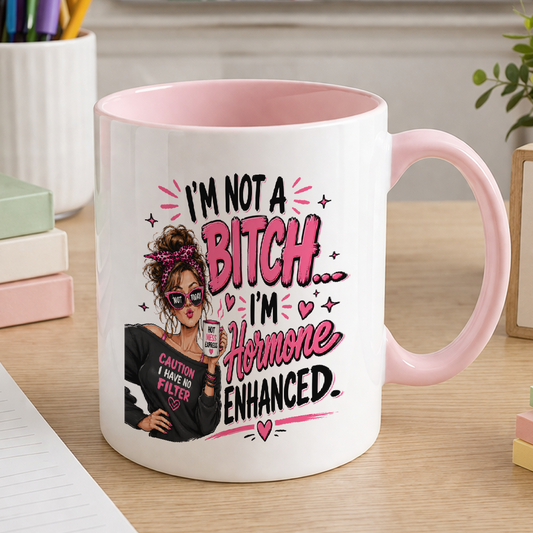 White ceramic mug with pink handle and pink inner, printed with an illustrated woman in sunglasses and the text I'm not a bitch, I'm hormone enhanced
