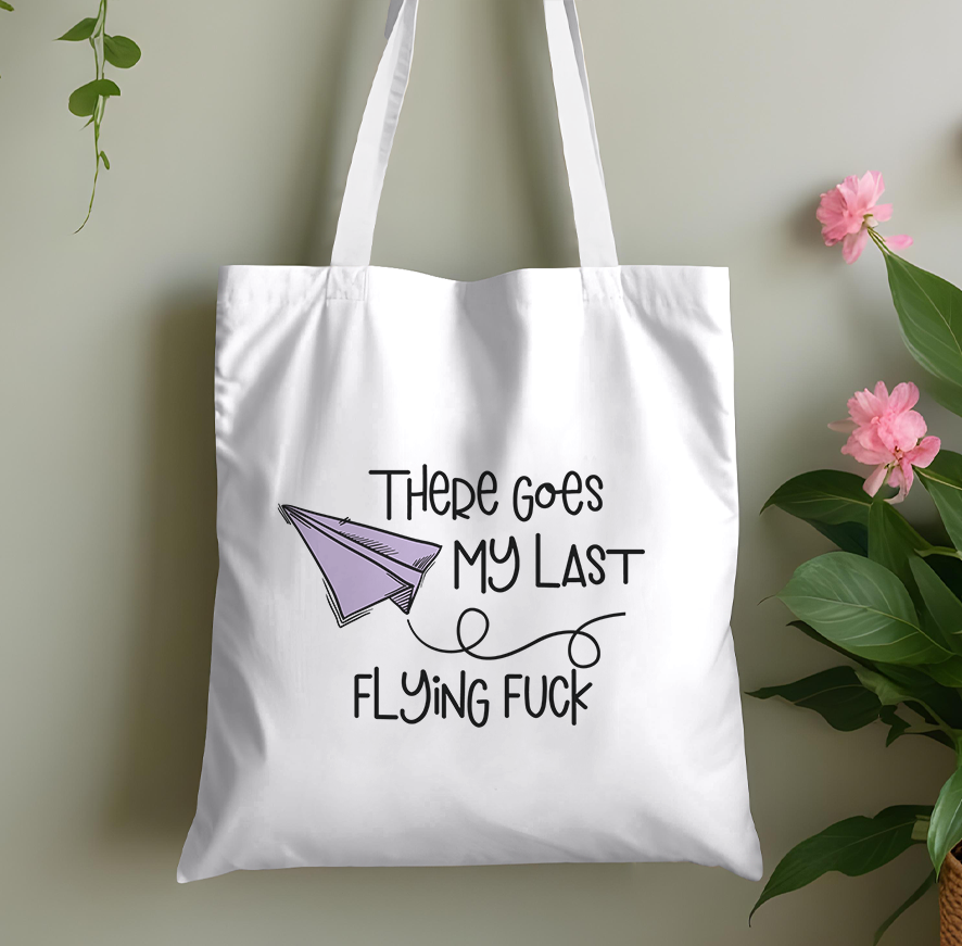 Plain pink cotton tote bag printed with a paper plane graphic and a cheeky adult-humour pun slogan, laid flat against a plain background