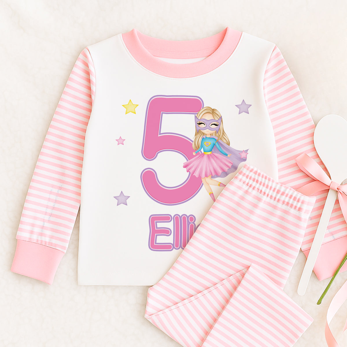 Pink and white striped pyjama set with a superhero girl graphic featuring a cape and star, personalised with a custom name on the top.
