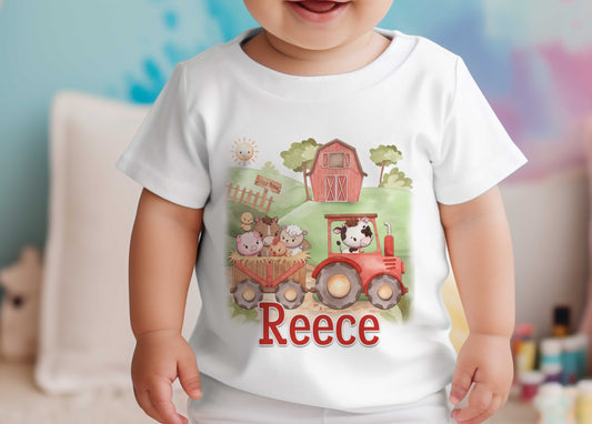 Toddler wearing a white T-shirt printed with a red tractor carrying farm animals and the personalised name Reece, against a blue background.