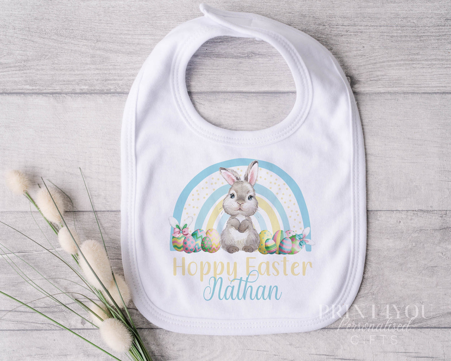 Personalised white cotton baby bib with Easter Bunny rabbit and blue and yellow rainbow design, custom name printed.