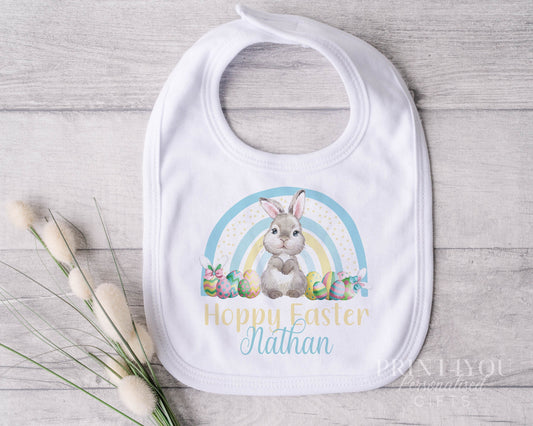 Personalised white cotton baby bib with Easter Bunny rabbit and blue and yellow rainbow design, custom name printed.