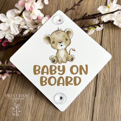 Baby on Board car window sign with baby lion cub design, propped against spring blossom on a wooden surface
