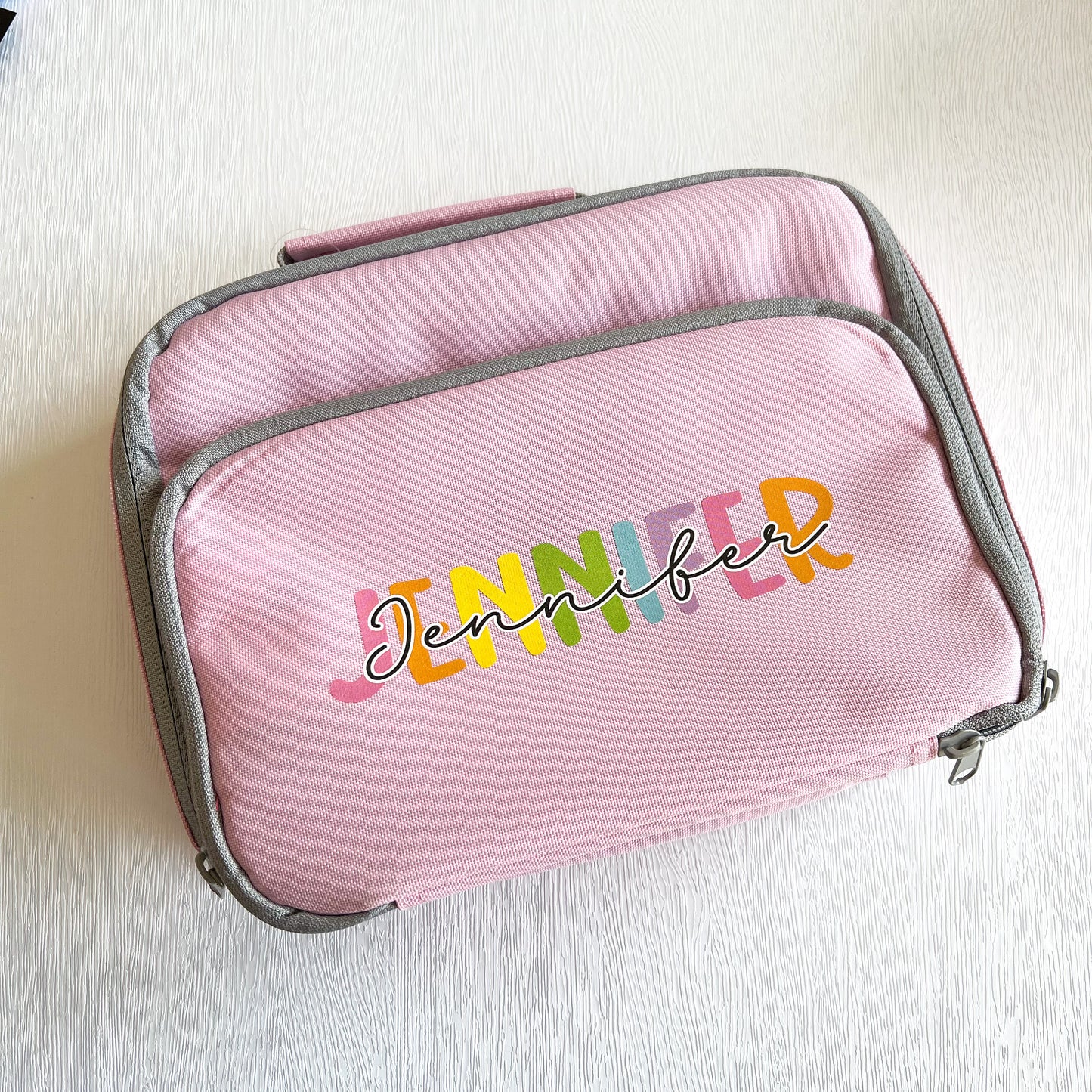 Pink insulated lunch cooler bag with front zip pocket, personalised with the colourful name Jennifer, top-down view.