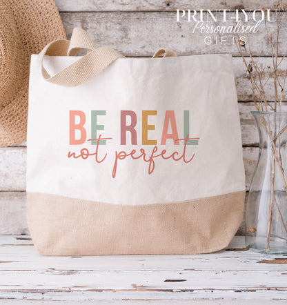 Cream and natural jute tote bag with a tan base and cotton handles, printed with a colourful 'Be Real Not Perfect' slogan design.
