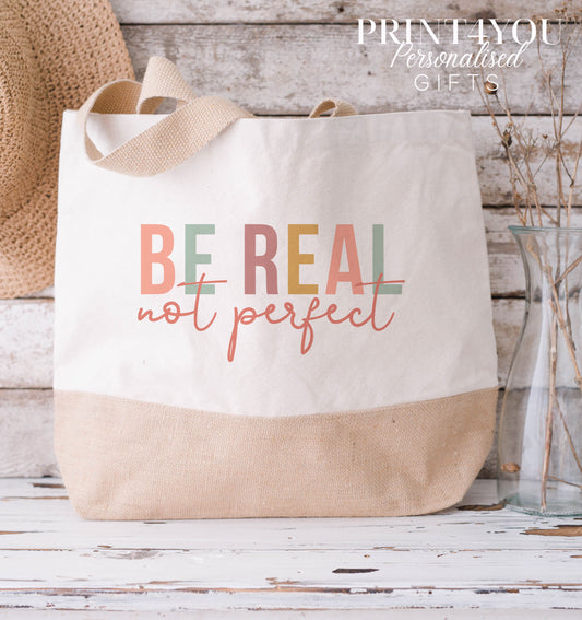 Cream and natural jute tote bag with a tan base and cotton handles, printed with a colourful 'Be Real Not Perfect' slogan design.