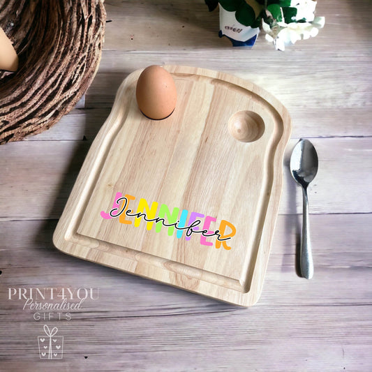 Wooden egg breakfast board printed with a rainbow-coloured personalised name 'Jennifer', shown with a boiled egg and spoon