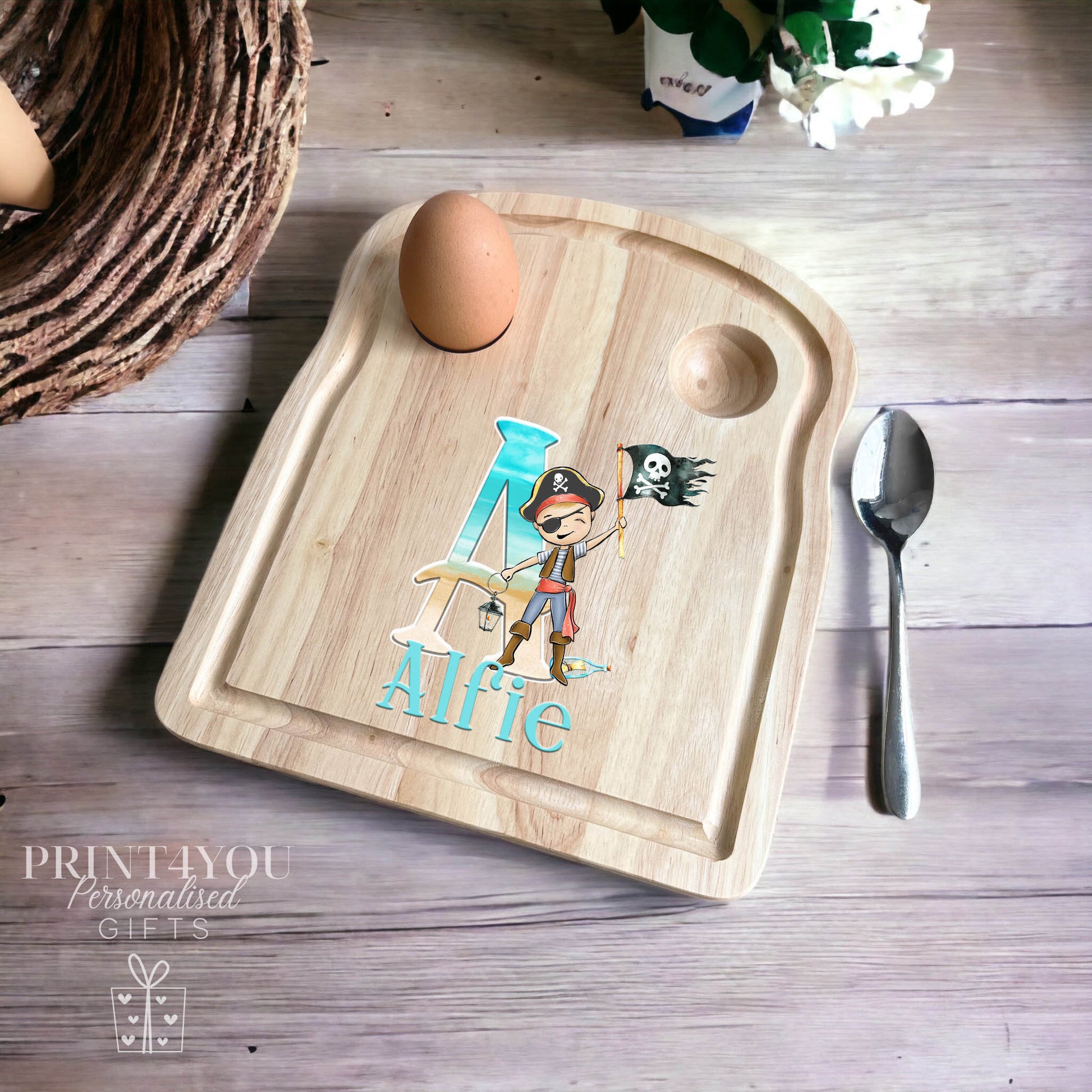 Wooden egg board with a carved egg cup and spoon rest, personalised with a large letter A, a cartoon pirate and the name Alfie.