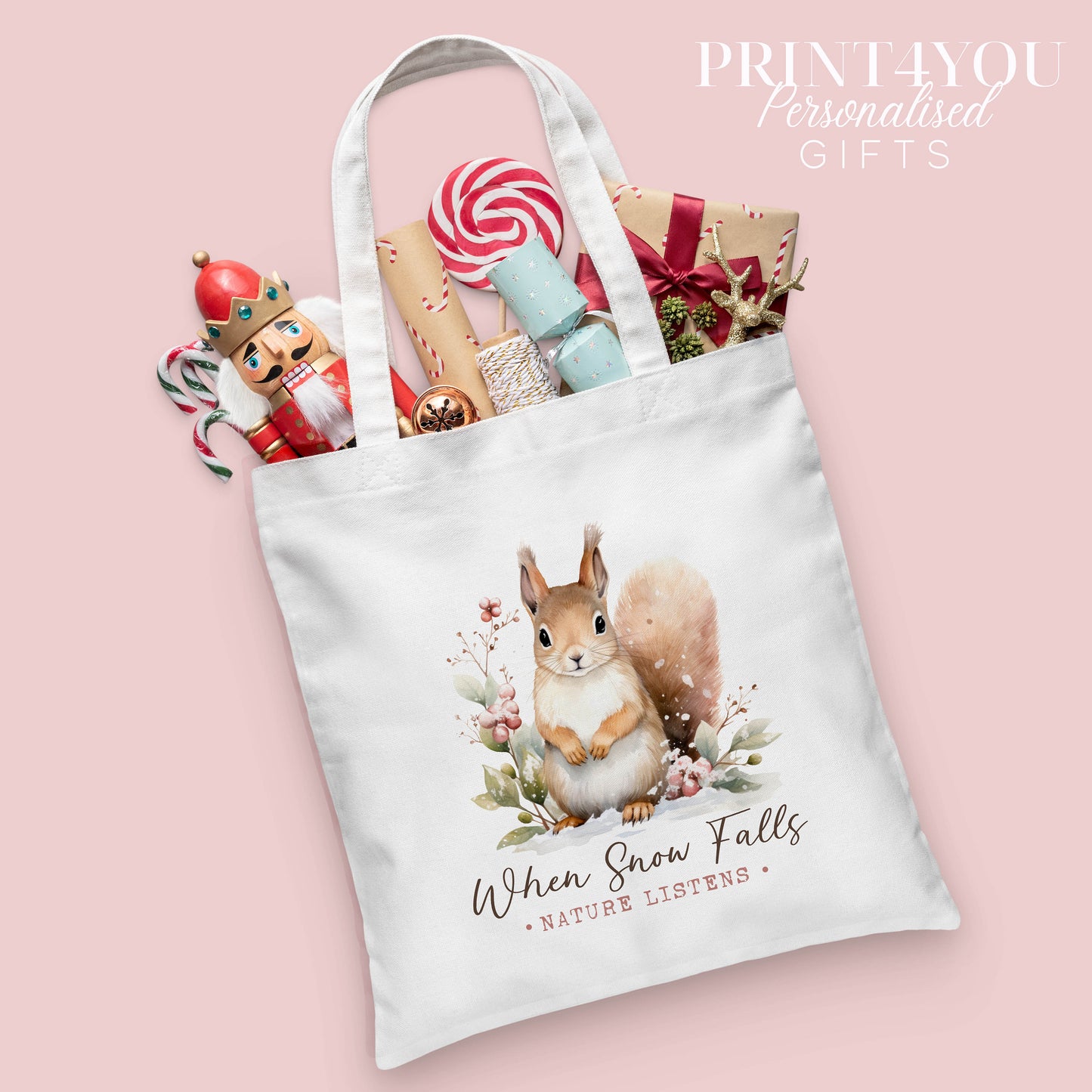Woodland squirrel Christmas cotton tote bag printed with the words 'When Snow Falls, Nature Listens', shown packed with festive nutcracker and gift wrap props