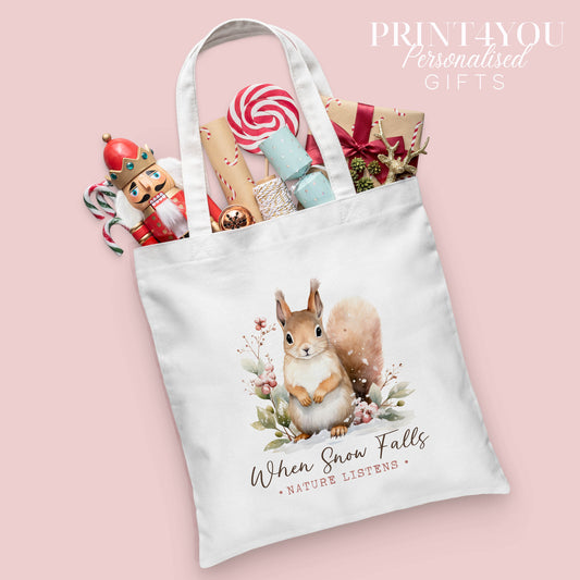 Woodland squirrel Christmas cotton tote bag printed with the words 'When Snow Falls, Nature Listens', shown packed with festive nutcracker and gift wrap props
