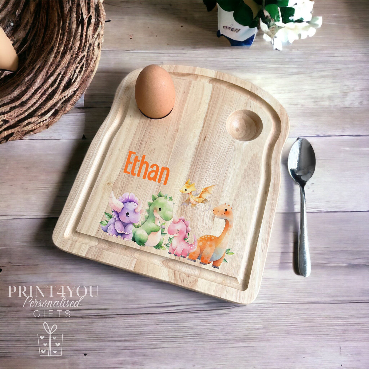 Personalised wooden egg breakfast board printed with a colourful mixed dinosaur design and the name 'Ethan', shown with a boiled egg, spoon and toast setting