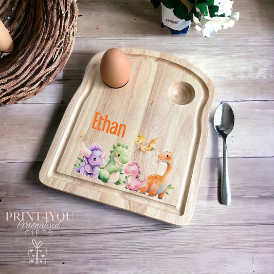 Personalised wooden egg breakfast board printed with a colourful mixed dinosaur design and the name 'Ethan', shown with a boiled egg, spoon and toast setting