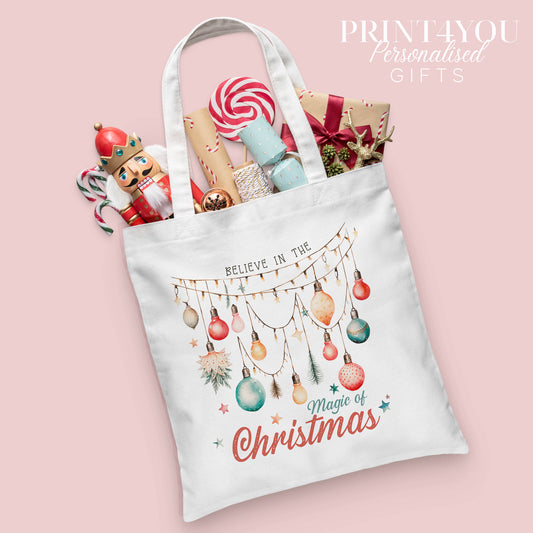 Christmas cotton tote bag printed with a fairy lights design and the words 'Believe in the Magic of Christmas', shown packed with festive nutcracker and gift wrap props